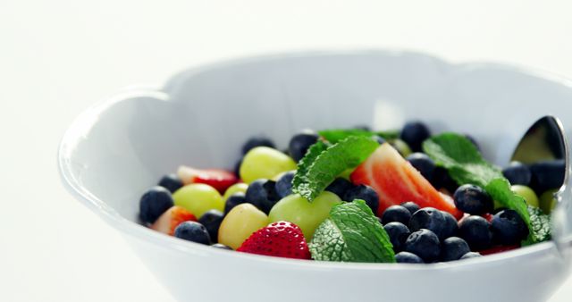 A vibrant mixed fruit salad featuring blueberries, strawberries, grapes, and mint leaves in a white bowl. Perfect for promoting healthy eating, summer recipes, vegetarian or vegan menu items, and nutrition articles.