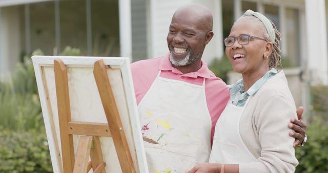 Senior African American couple engaging in outdoor painting, creating art and enjoying quality time together. They are smiling and appear happy, embodying relaxation and creativity in a natural environment. Great for topics related to retirement lifestyles, senior activities, togetherness, and artistic hobbies.