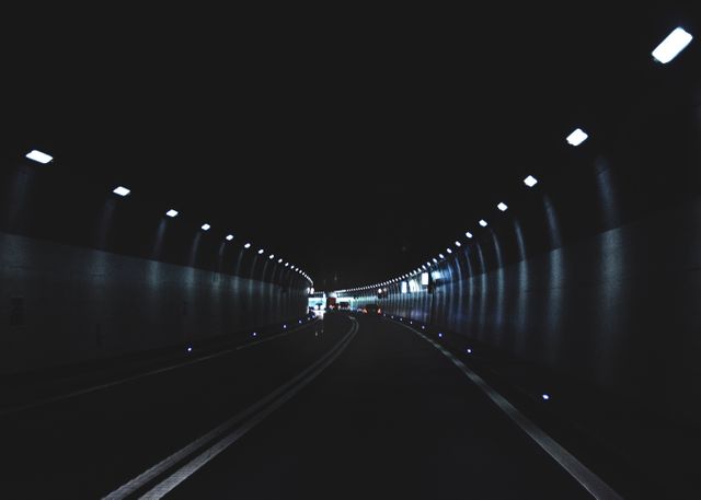 This dark tunnel with a curved road and dim lighting represents urban transportation and infrastructure. It evokes themes of solitude and focus, making it ideal for illustrating concepts related to travel, commuting, and modern road networks. This image could be used in articles or content about engineering, urban planning, or journey kinematics. It also works well for conveying eerie or introspective atmospheres in editorial, commercial, and artistic contexts.