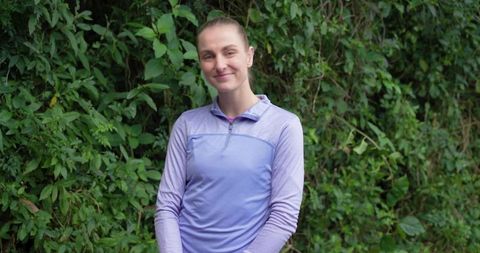 Smiling woman standing in front of green hedge wearing lavender quarter-zip athletic pullover
