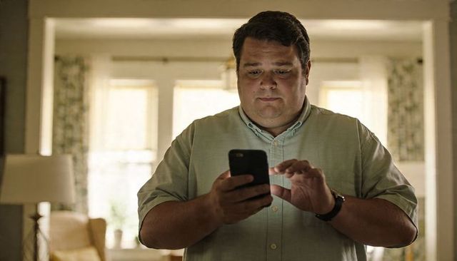 Middle-aged man using smartphone in cozy living room soft natural light checking messages