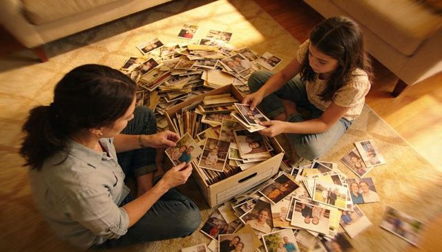 Mother and daughter sorting vintage family prints on living room rug with archive box
