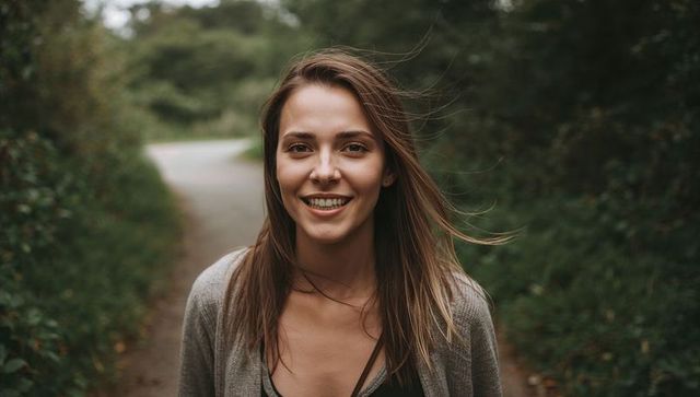Smiling woman standing on trail wearing gray cardigan and thin necklace natural portrait