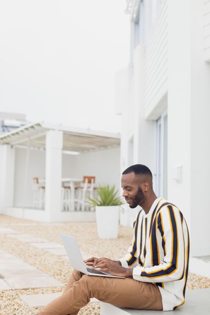 Side view of an African-American man using a laptop while sitting outdoors by the pool