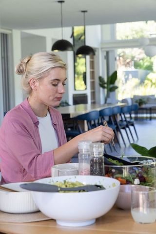 Blonde woman serving fresh salad at modern open-plan dining table casual bright kitchen
