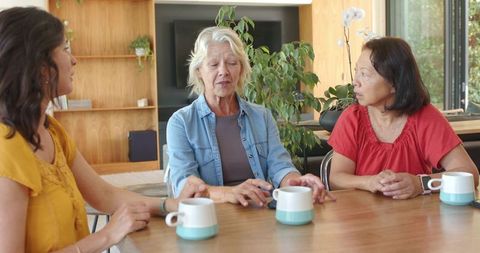 Diverse friends enjoying coffee while senior woman sharing stories at sunny kitchen table