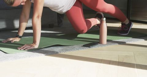 Woman doing core plank workout on yoga mat at home with water bottle and phone