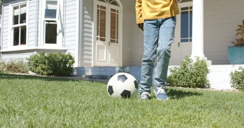African american child standing with soccer ball on sunny suburban front lawn