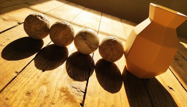 Golden sunlit still life with marble orb, clay spheres and faceted pitcher on wood planks