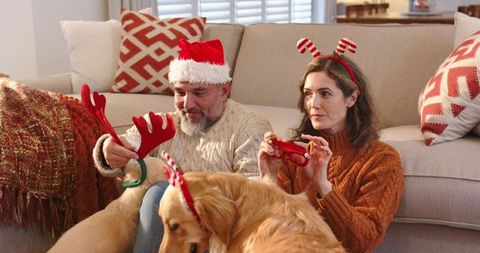 Mature Couple Wearing Santa Hat and Reindeer Antlers Playing with Retriever at Home