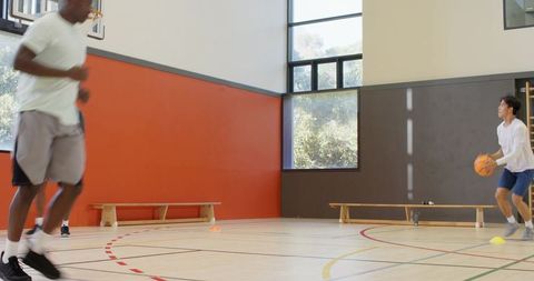 Diverse male basketball players practicing passing and shooting team drills in indoor gym