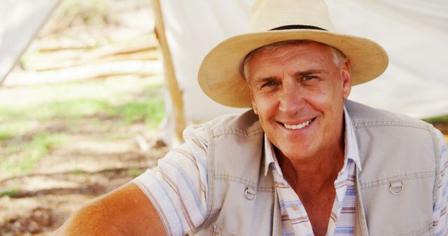 Elderly man wearing a straw hat and casual clothing smiling in an outdoor setting. Perfect for use in lifestyle blogs, retirement brochures, outdoor activity promotions, and senior health resources.