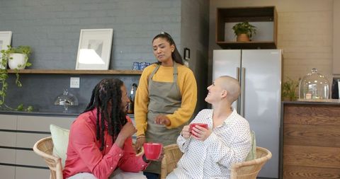 Barista serving two customers enjoying coffee in cozy modern cafe with plants