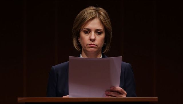 Female speaker reading speech at podium under spotlight in formal business attire