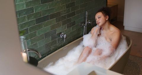 African american woman soaking in bubble bath relaxing with candlelight and green tile