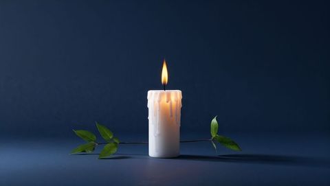 Glowing white pillar candle with green branch on blue background