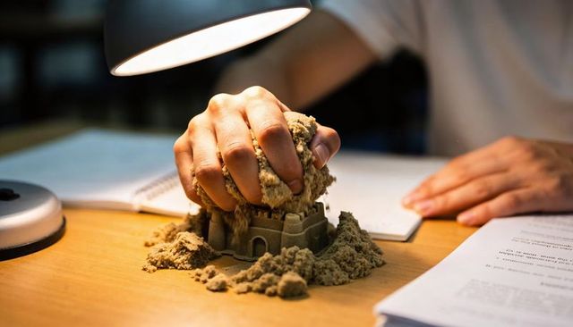Pressing kinetic sand into sandcastle mold on desk under warm lamp light