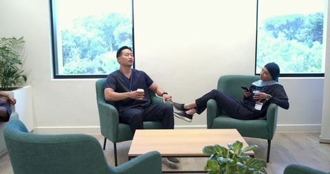 Multicultural healthcare staff relaxing in modern breakroom holding coffee and smartphones