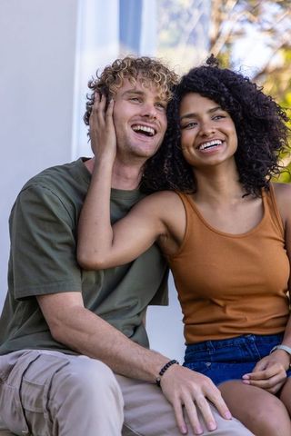 Laughing interracial couple sitting on porch steps sharing tender, sunlit romantic moment