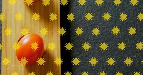 Resting glossy cherry tomato on bamboo board with yellow burst pattern and slate counter
