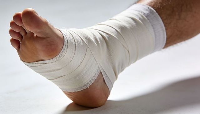 Elastic bandaged ankle and bare foot resting on white surface for medical first aid