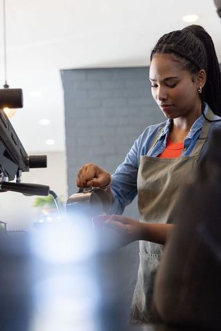 African american barista pouring steamed milk into latte cup creating latte art in cafe