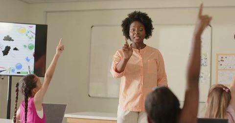 Female teacher engaging students raising hands in interactive classroom lesson with laptop