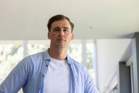 Adult man standing in modern sunlit room wearing casual light blue shirt and white tee