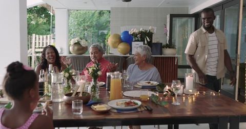 Multi-generational family sharing alfresco dinner on patio, laughing and passing juice