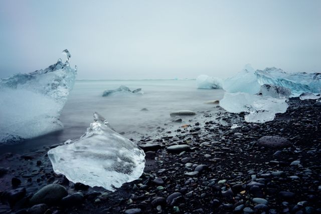 Misty shoreline features icy sculptures and smooth stones, suggesting a desolate, rugged, cold outdoor scene perfect for winter travel brochures, nature blogs, or weather reports.