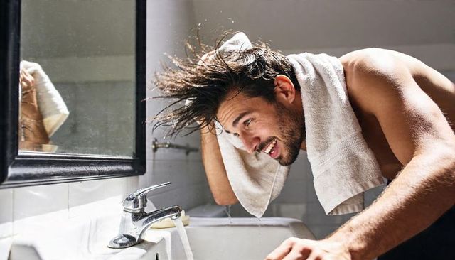 Young man drying hair at bathroom sink with towel morning grooming routine