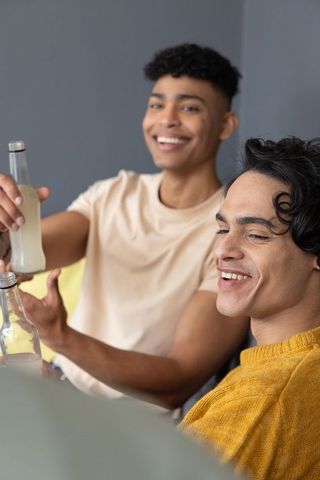Toasting bottled drinks on couch, teenage friends enjoying relaxed cozy home hangout moment