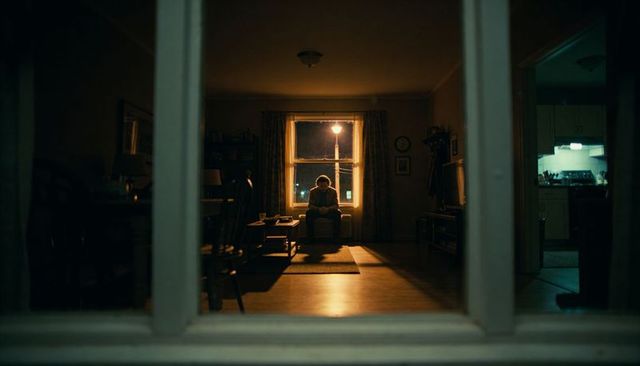 Lonely silhouette sitting by window under streetlight with warm lamp casting shadows in moody apartm