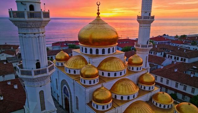 Golden-domed coastal mosque at sunset with white minarets overlooking calm sea