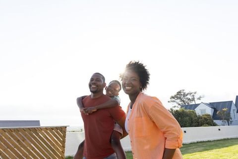 Smiling african american family walking on sunny suburban lawn carrying child on back