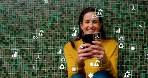 Smiling woman holding phone by green mosaic wall showing eco fintech icons and charts