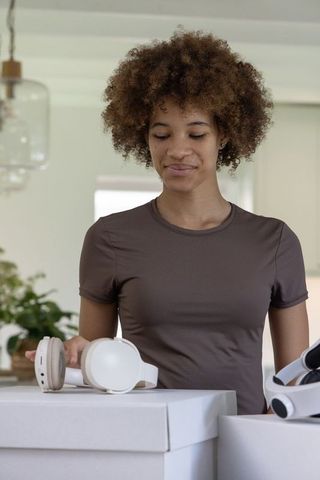African american woman unpacking white over-ear headphones from boxes in modern kitchen