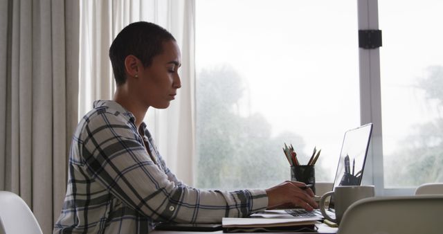 Focused person with short hair working on laptop at gray table near window - Download Free Stock Images Pikwizard.com