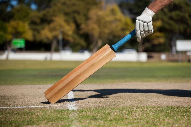 Close-up of a cricket player scoring a run on a cricket field, with a bat and gloved hand visible. Ideal for use in sports-related content, articles about cricket, athletic training materials, and promotional materials for cricket events.