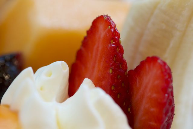 Close-up of fresh strawberries alongside whipped cream and banana slices. Ideal for food blogs, dessert recipes, and healthy eating promotions. Suitable for illustrating fresh fruit, taste profiles, and appetizing dessert presentations.