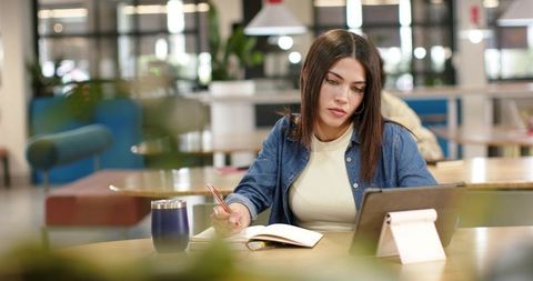 African american woman studying in coworking space using tablet and writing notes