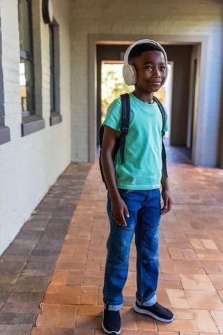 African american boy listening to music wearing headphones and backpack on brick walkway