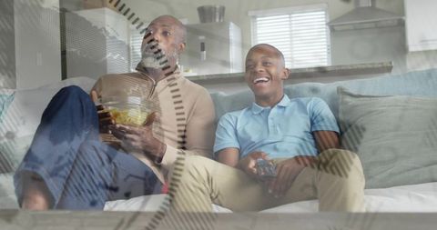 Father and teen son laughing while watching tv on sofa, casual home bonding weekend moment