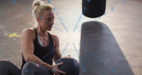 Blonde woman training with medicine ball in gym with augmented blue data overlay