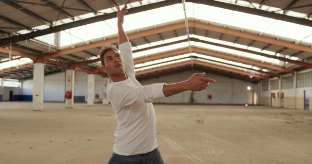 Focused caucasian male dancer dancing in abandoned sunny warehouse. Dance, urban lifestyle and movement, unaltered.