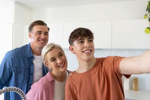 Teen taking selfie with smiling parents in bright modern kitchen, family bonding moment