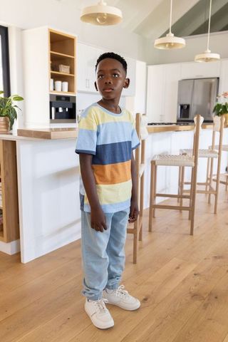 African american boy standing in bright modern kitchen wearing striped tee looking right