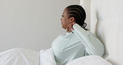 African american woman sitting up in bed adjusting mint top for morning relaxation