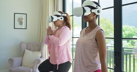 African american women practicing vr yoga at home wearing smartwatches, daylight balcony