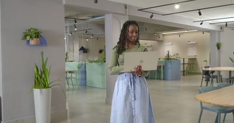 African woman using laptop in modern coworking space with plants and minimalist design